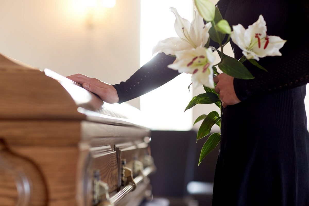 Funeral undertakers hand with flowers in hand placed on top of wooden oak coffin